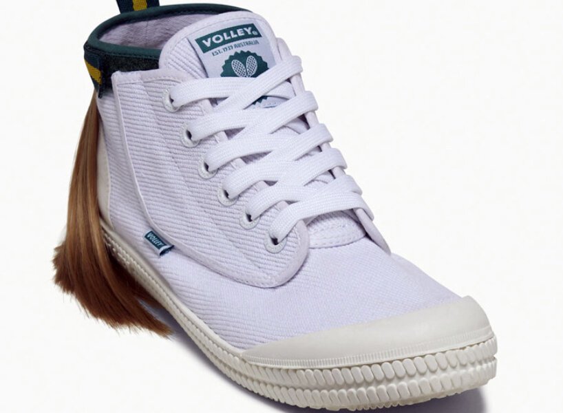 isso é um sapato com um mullet designboom volley (2) Tênis todo branco com uma mecha de cabelo presa na parte superior traseira, simulando um mullet. O cabelo é preso por uma tira de velcro que por fora é verde com uma listra amarela.