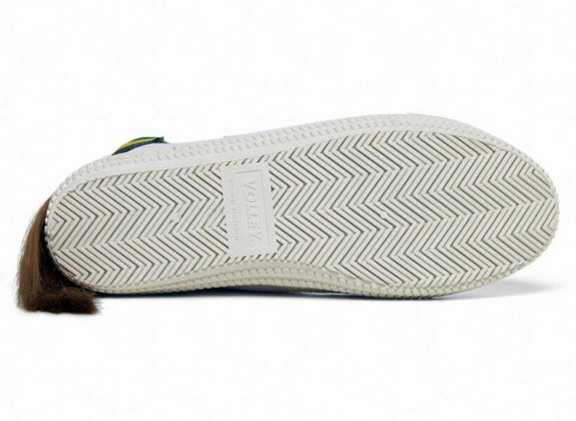 isso é um sapato com um mullet designboom volley (6) Tênis todo branco com uma mecha de cabelo presa na parte superior traseira, simulando um mullet. O cabelo é preso por uma tira de velcro que por fora é verde com uma listra amarela.