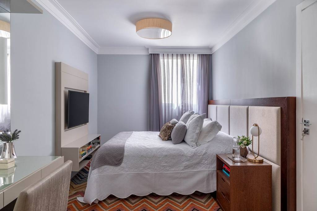 moveis-usados-nova-decoracao5 Cama com acolchoado branco, janela com cortina cinza, paredes azuis, televisão presa a um painel.