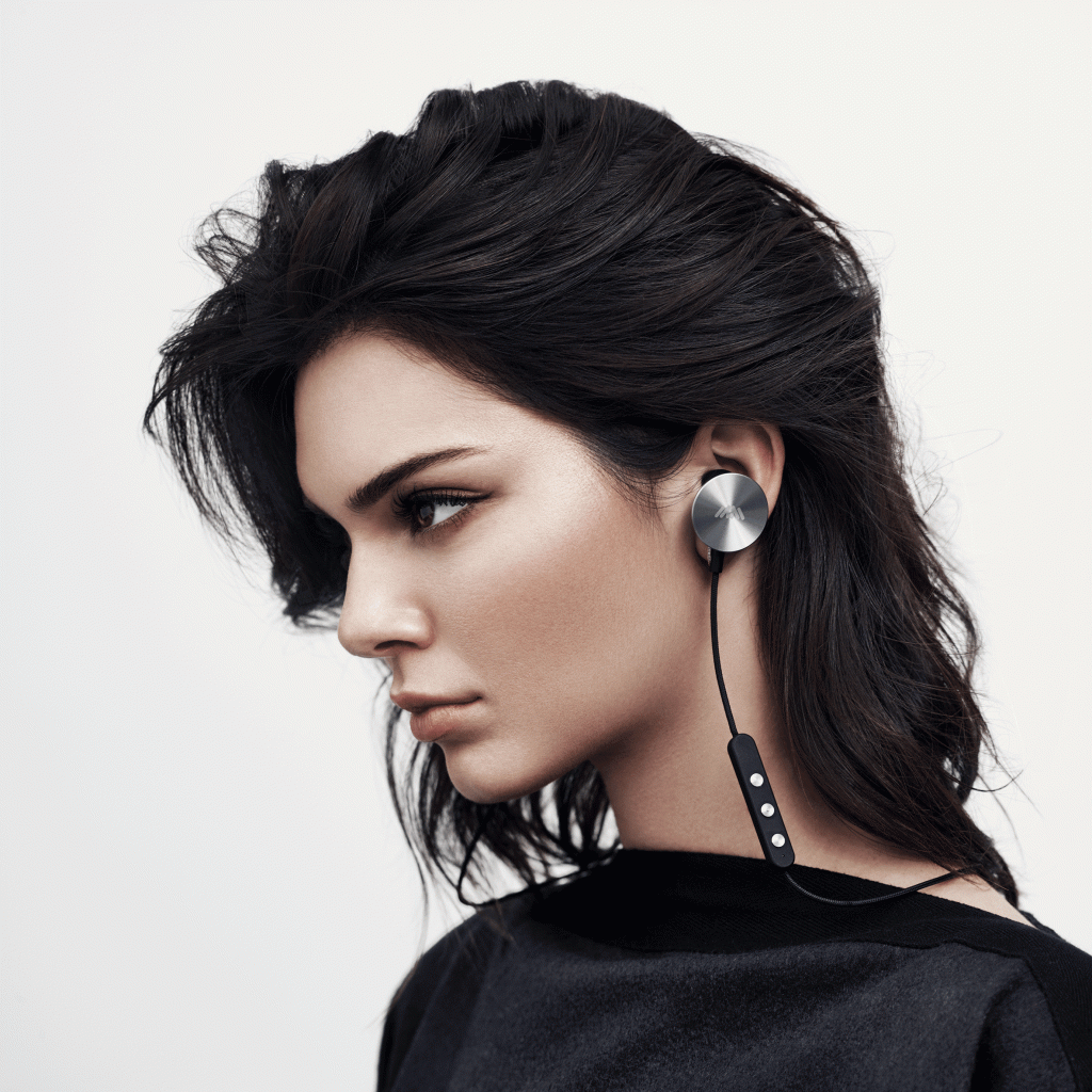 10 peças de design criadas por celebridades Dezeen (1) Mulher jovem usa fones de ouvido intra-auriculares com parte externa acabadas em metal escovado.