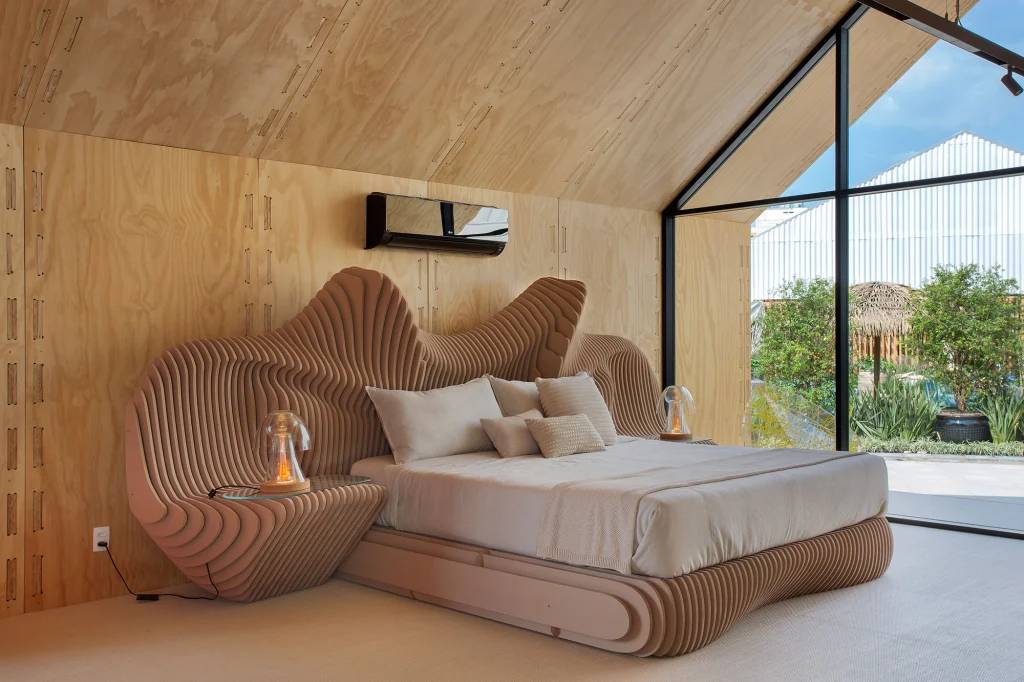 3-vantagens-da-madeira-engenheirada-renato-navarro-casacor-cama-clc-guto-requena Quarto com cama de casal desenhada em madeira engenheirada em formato orgânico, com paredes de madeira e abertura de vidro.
