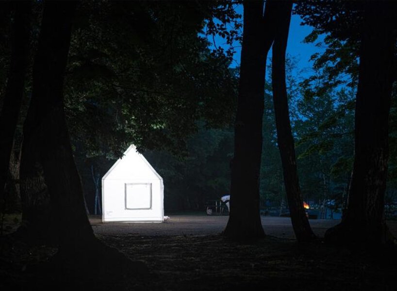 Conheça esta casinha de acampamento inflável Tsutaya Electrics (6) Casa inflável branca brilhando na escuridão de uma bosque à noite.