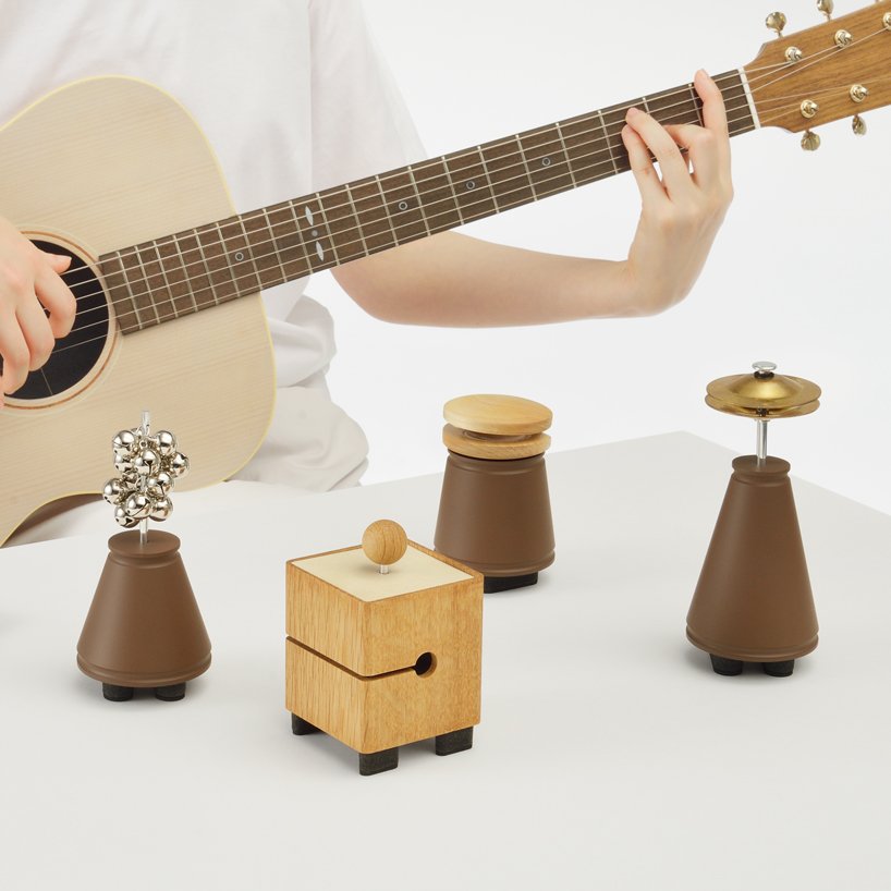 Esses acessórios de música interagem com seu celular Designboom Yamaha música (2) Pessoa toca violão em frente a mesa sobre a qual jazem 4 pequenos objetos de madeira de diversos formatos.
