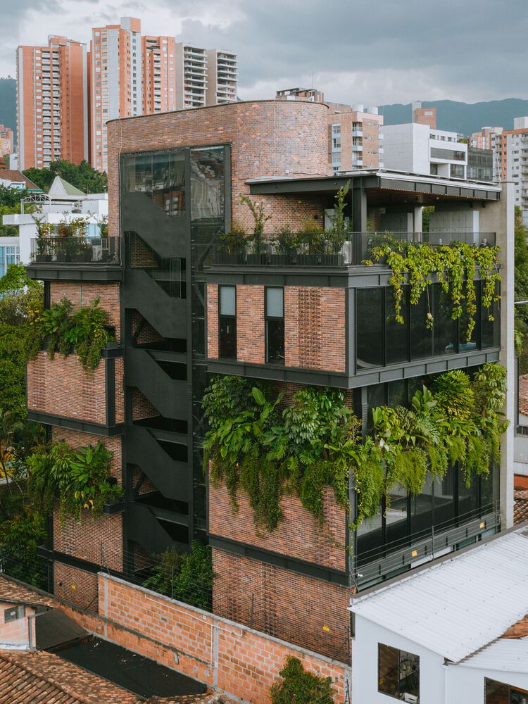 edificio-corporativo-medellin-arquitetura-acolhedora-mateo-soto-fachada-floreiras-metalica-tijolinho Fachada de prédio com estrutura metálica, tijolinhos aparentes e floreiras com vegetação densa.