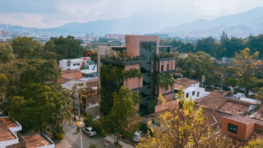 Fachada de prédio em destaque na paisagem do bairro, com montanha ao fundo.