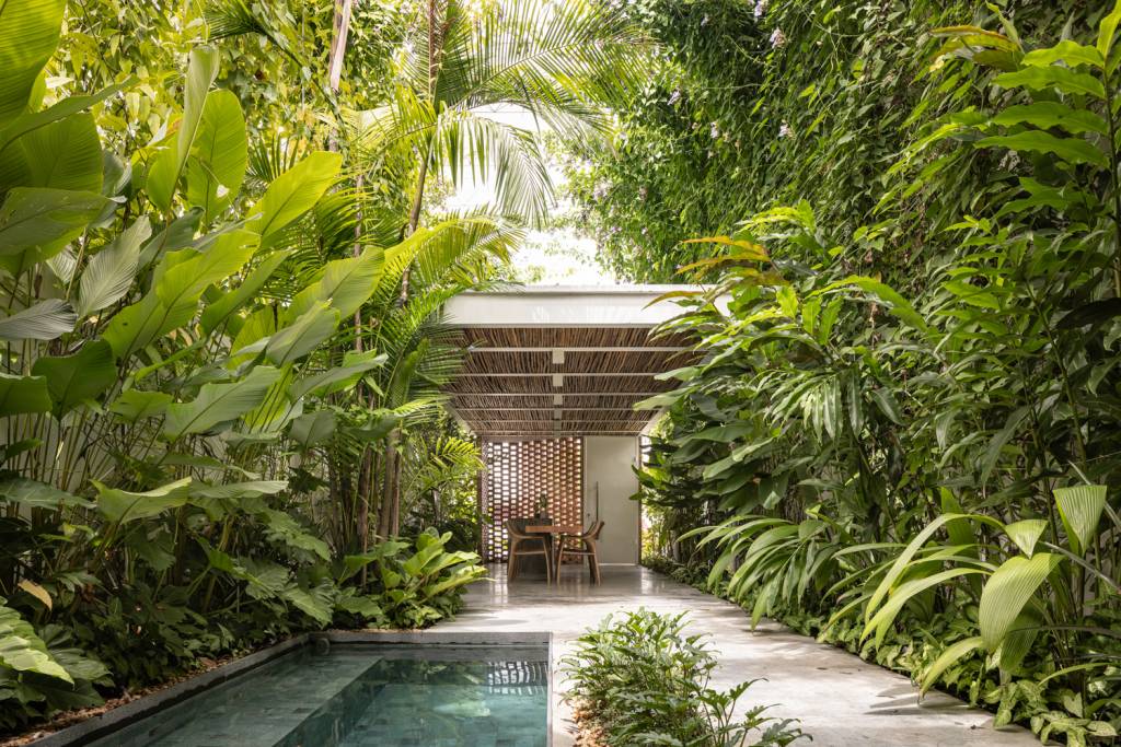 fachada-vazada-de-tijolos-marca-escritório-manaus-Joana-França-área-gourmet-externa-piscina-jardim Em primeiro plano vemos a piscina, ladeada por plantas tropicais e, ao fundo, uma cozinha gourmet que também serve como lugar para reuniões.