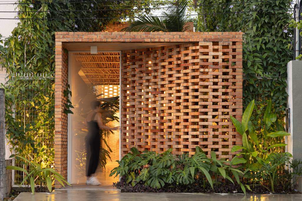 fachada-vazada-de-tijolos-marca-escritório-manaus-Joana-França-detalhe-da-entrada-jardim Detalhe da entrada do escritório, em fachada vazada de tijolos, com porta branca à esquerda.
