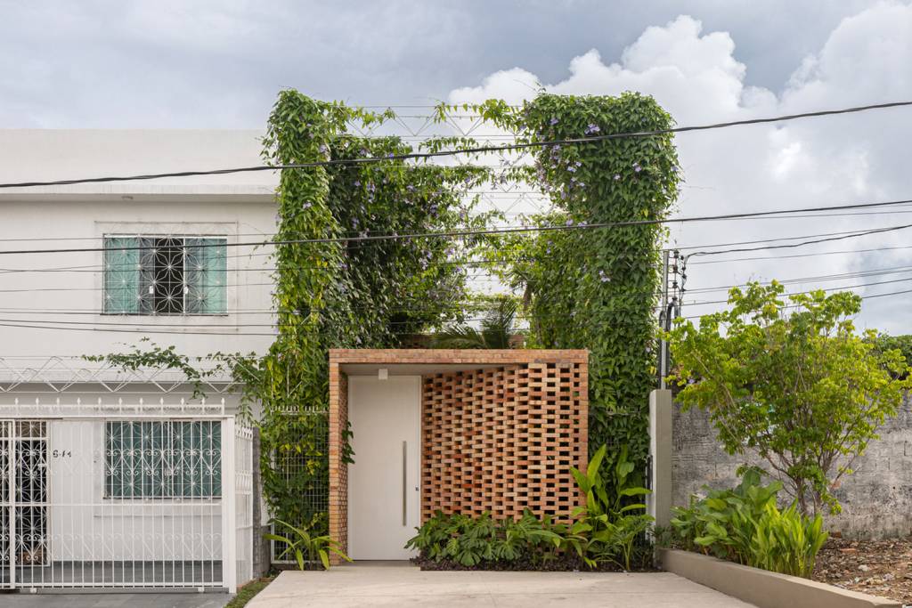 fachada-vazada-de-tijolos-marca-escritório-manaus-Joana-França-fachada-frontal-trepadeiras-galpão Fachada do escritório visto da rua, com pórtico de tijolos vazados e, acima, um