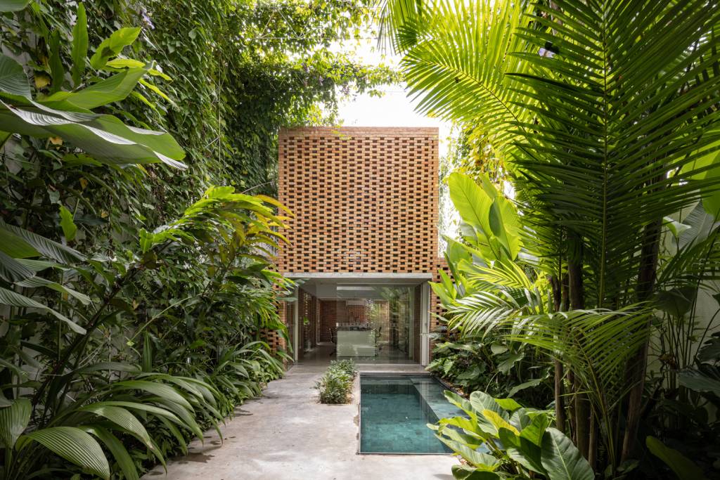 Cercada de plantas, escritório tem tijolos vazados na fachada posterior, virada para a piscina.
