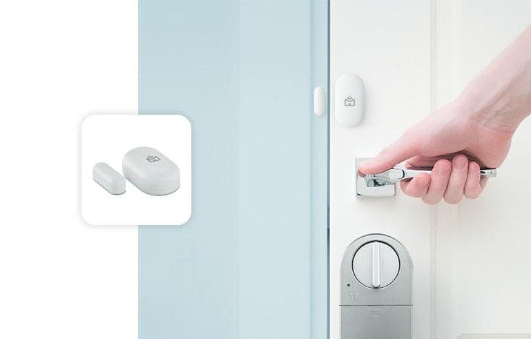 Pequeno sensor de abertura da Positivo Casa Inteligente que consiste em duas pequenas cápsulas brancas que devem ser fixadas alinhas na porta e no batente.