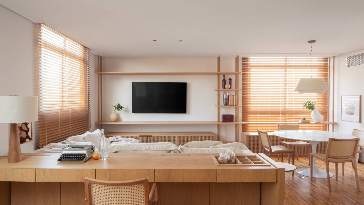 Sala com estante em madeira e sofá; Bancada de home office atrás do sofá