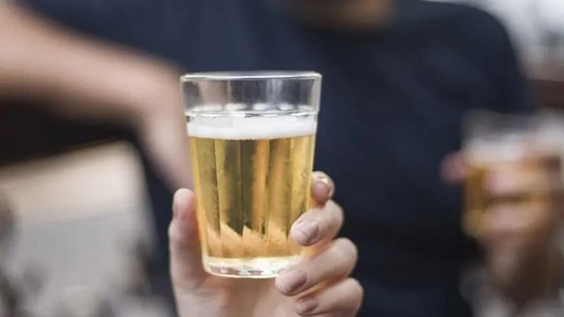 Mão segurando copo americano com cerveja