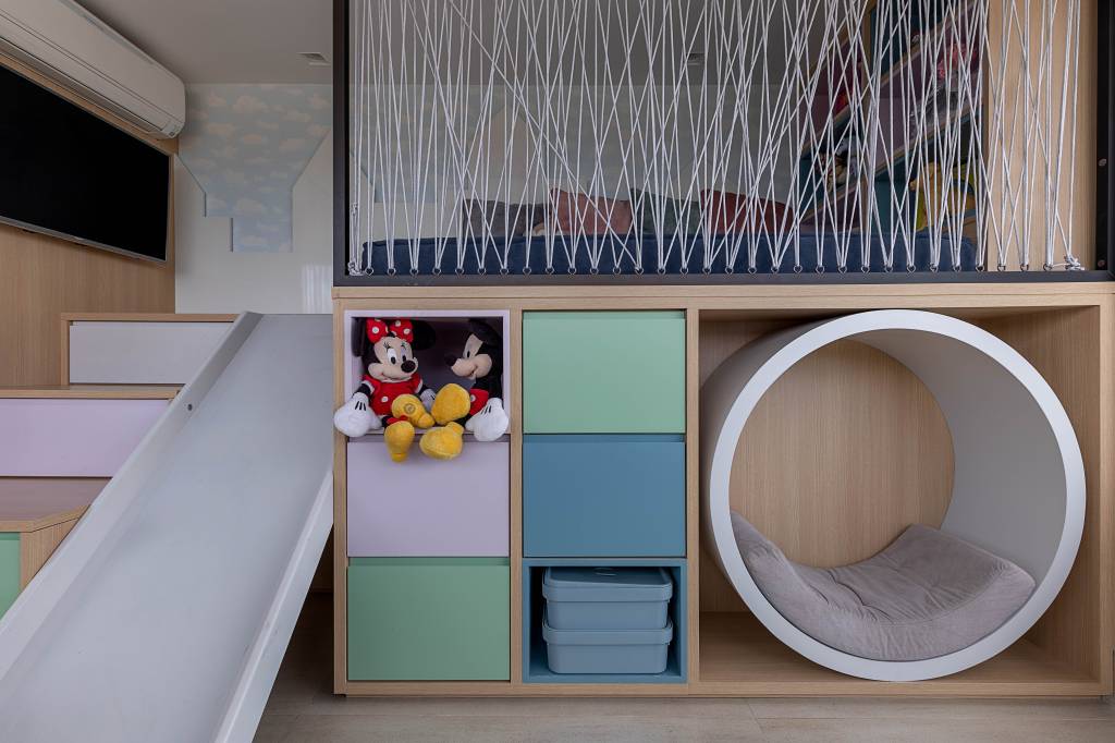 quarto-crianca-projeto-norah-carneiro-credito-rafael-renzo-01 Na premissa de criar um ambiente divertido, lúdico e organizado, a designer de interiores Norah Carneiro desenvolveu um espaço kids com caixas organizadoras, gavetas coloridas na escada e, para garantir a diversão, foi atribuído em meio a marcenaria personalizada um escorregador. Na parte alta da estrutura, a profissional inseriu papel de parede com céu azul e um recorte em relevo de castelos, além de outros nichos para organizar os brinquedos.