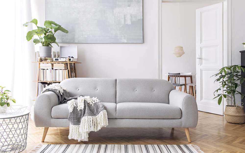sala-sofa-plantas-the-home-depot Inverno chegando: saiba como preparar a sua casa. Na foto, uma sala com sofá cinza, plantas e tapete listrado.