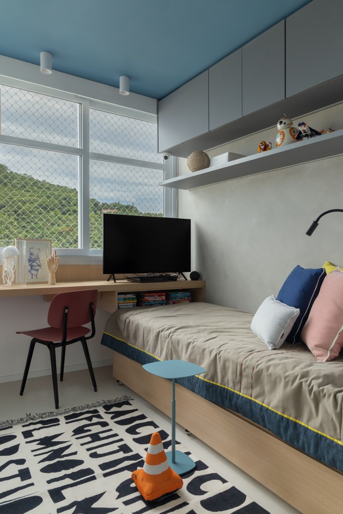 Quarto infantil com cama de solteiro e bancada para estudos; tapete estampado