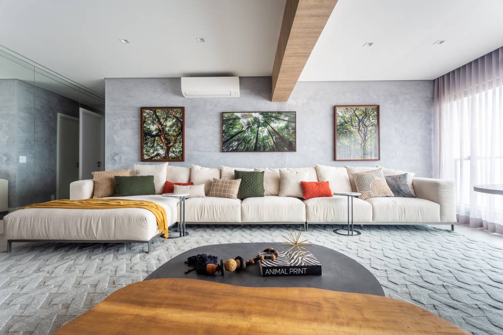 ape-95m-decoracao-influencia-nordestina-biofilia-llarquitetura-04-sala-sofa Sala de estar com sofá branco grande, parede de cimento queimado e fotografias de árvores.