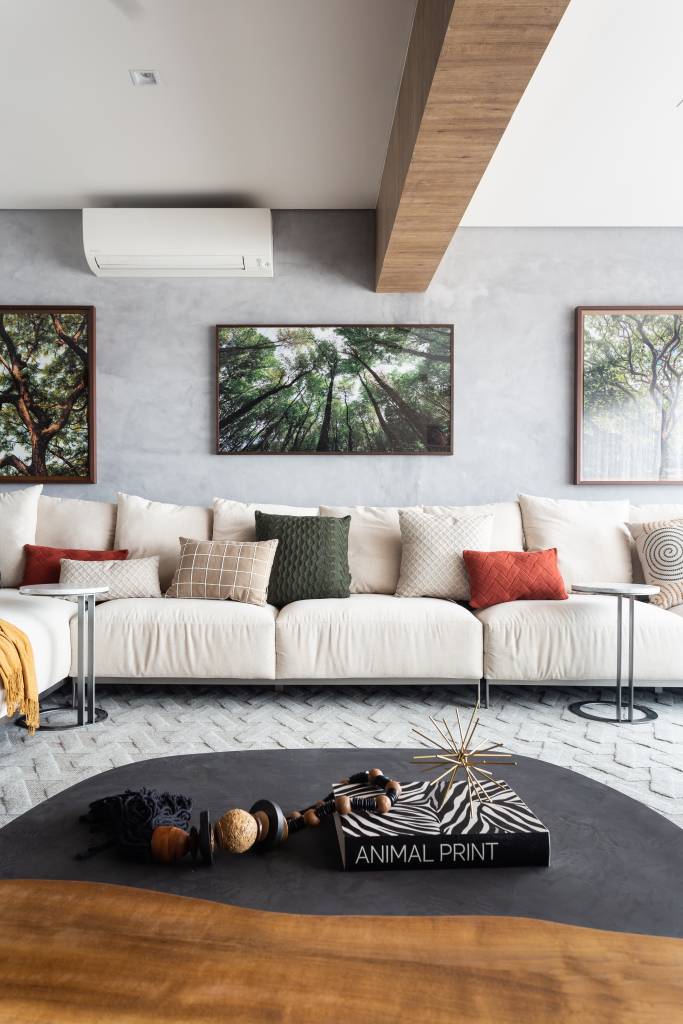 ape-95m-decoracao-influencia-nordestina-biofilia-llarquitetura-05-sala-sofa Sala de estar com sofá branco grande, parede de cimento queimado e fotografias de árvores.