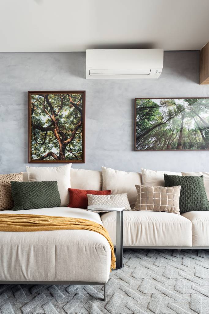 ape-95m-decoracao-influencia-nordestina-biofilia-llarquitetura-06-sala-sofa Sala de estar com sofá branco grande, parede de cimento queimado e fotografias de árvores.