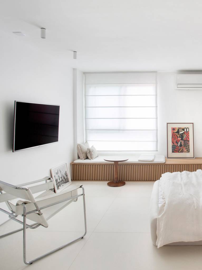 ape-40m-transformado-loft-minimalista-diego-raposo-arquitetos-02-poltrona-branco Loft branco com cama branca baixa e banco de madeira ripada