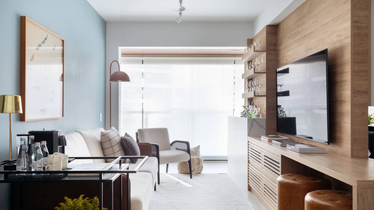 Sala de estar pequena com parede azul, sofá branco, poltrona branca e bar integrado.