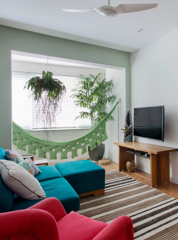 Sala de estar pequena com sofá azul turquesa, tapete listrado e rede.