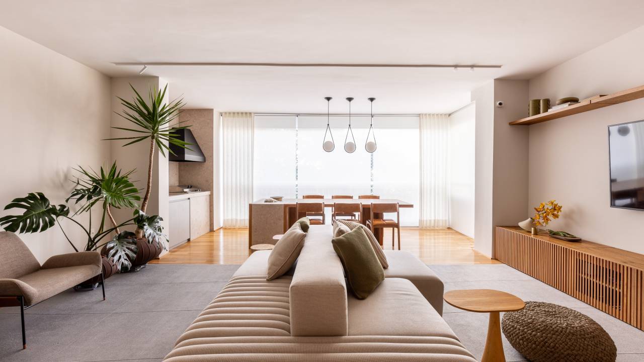 Sala integrada com varanda em tons neutros; sofá ilha claro e plantas.