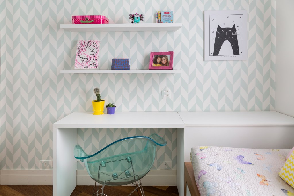 Quarto infantil com bancada de estudos branca e papel de parede geométrico.