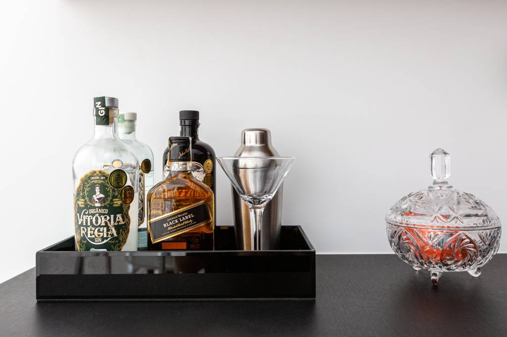 Home bar com bancada preta e bandeja preta de bebidas.