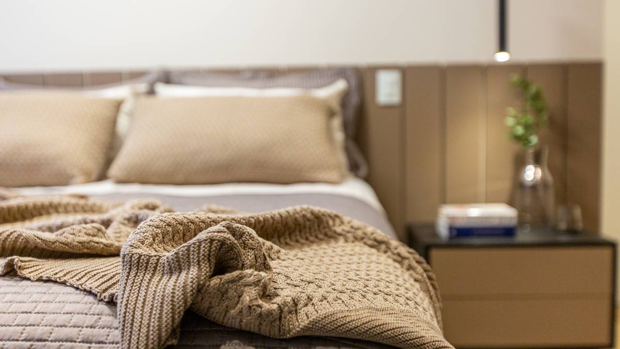 Quarto com cama de casal; almofadas e manta beges.