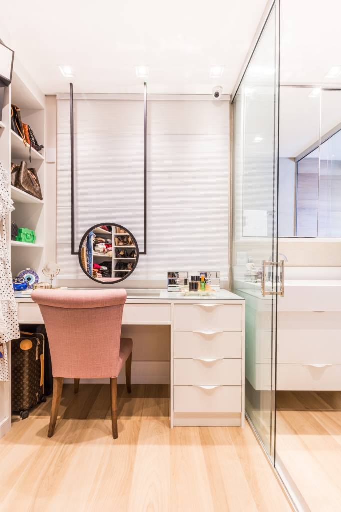 painel-com-duas-tvs-lareira-ambientes-integrados-ape-daniela-funari-06-closet-penteadeira Closet com penteadeira; cadeira rosa, bancada branca e espelho redondo.