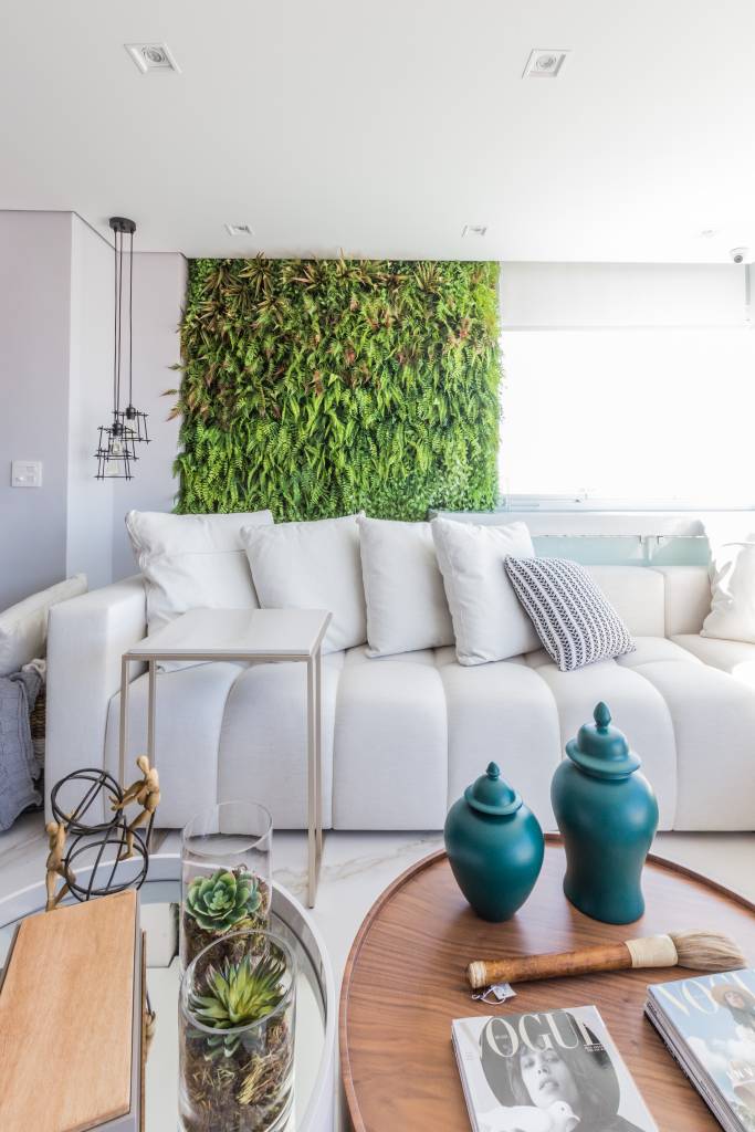 painel-com-duas-tvs-lareira-ambientes-integrados-ape-daniela-funari-25-sofa-varanda-jardim-vertical Varanda integrada com sofá branco e jardim vertical.