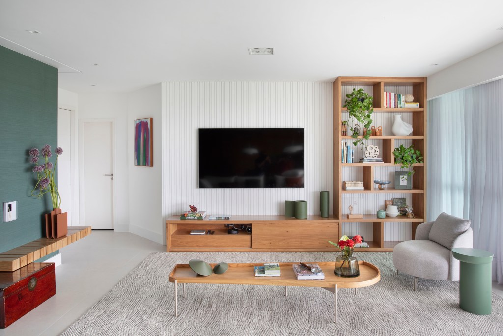 Sala de tv com sofá claro e estante vazada com plantas.