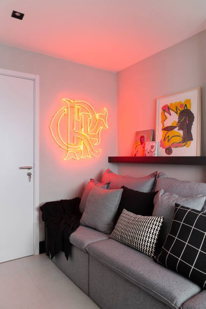 Quarto de hóspedes com sofá cinza grande e luminária neon do flamengo.