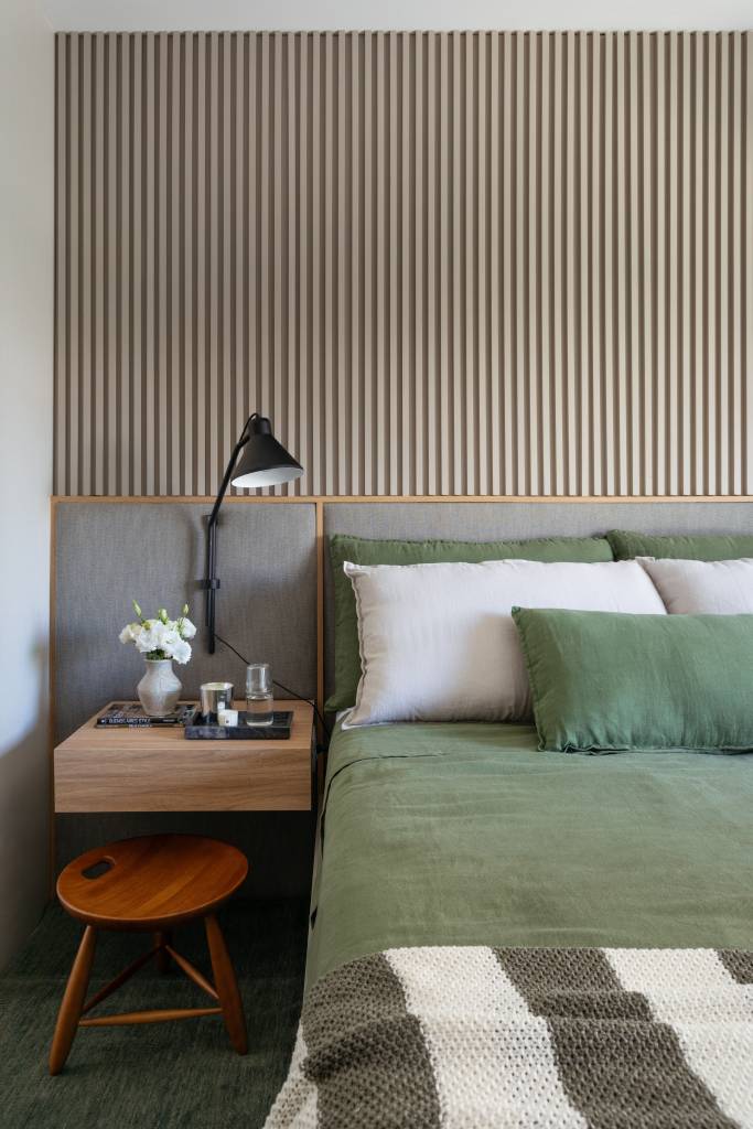 reforma-decor-sobrio-tons-de-cinza-ape-100m-rodolfo-consoli-12-quarto Quarto com cama de casal e roupa de cama verde; cabeceira estofada e parede revestida com painel ripado.