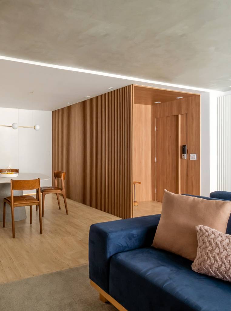 toques-de-azul-referencia-mar-ape-elegante-160m-studio-plano-arquitetura-02 Sala de jantar com madeira; mesa redonda, cadeiras de madeira, sofá azul.