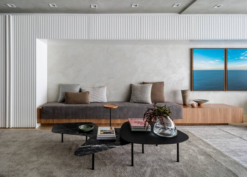 toques-de-azul-referencia-mar-ape-elegante-160m-studio-plano-arquitetura-13 Sala de estar revestida de cimento queimado com banco de madeira e estante de marcenaria branca.