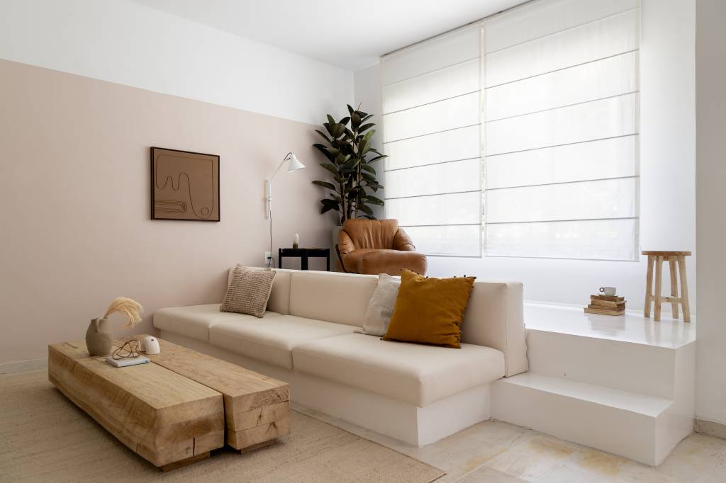 ape-100m-decor-natural-cantinho-de-leitura-isabella-lucena-14-sofa Sala de tv em tons claros com rack branco, sofá branco e mesa de centro de madeira rústica; degrau embaixo de janela para cantinho de leitura.