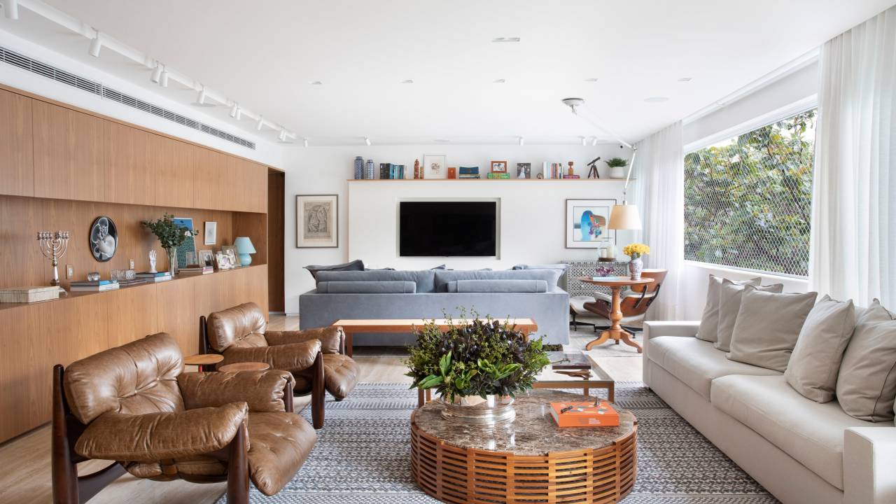 Sala de estar clara com tapete azul, sofá branco, poltronas Moles e sala de tv com sofá azul