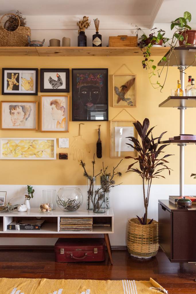Sala de estar com meia parede amarela, aparador pequeno branco e gallery wall.