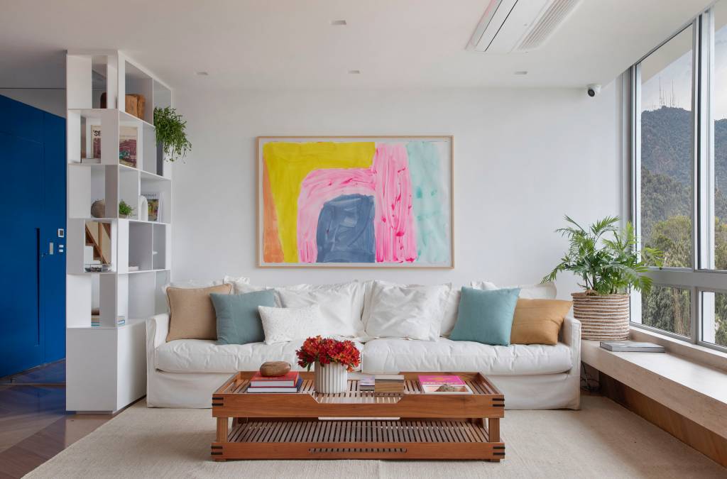 cobertura-260m-gramado-natural-escala-arquitetura-18-sala-sofa Sala de estar com sofá branco, tapete bege, poltrona e quadro colorido.