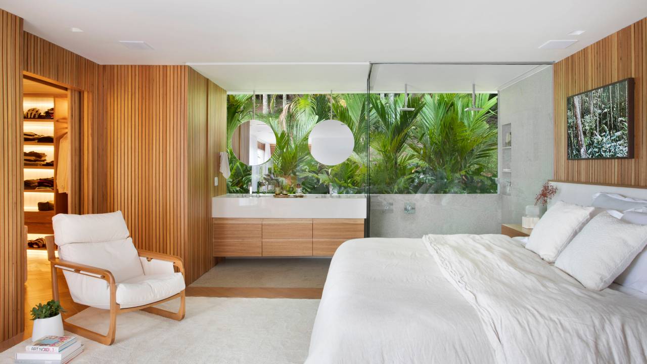 Suíte branca com vista para jardim; banheiro com espelhos redondos e bancada para casal.