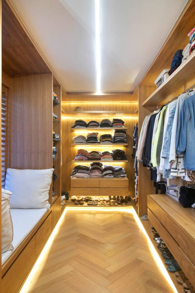 Closet com armários em madeira e prateleiras iluminadas.