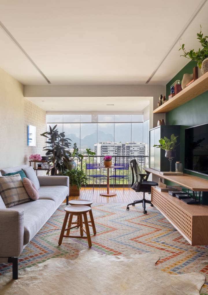 ape-110m-decoracao-contemporanea-toques-retro-kelly-figueiredo-01-sala-varanda-tapete Sala de estar integrada com varanda e jantar; tapete colorido, sofá cinza e parede verde.