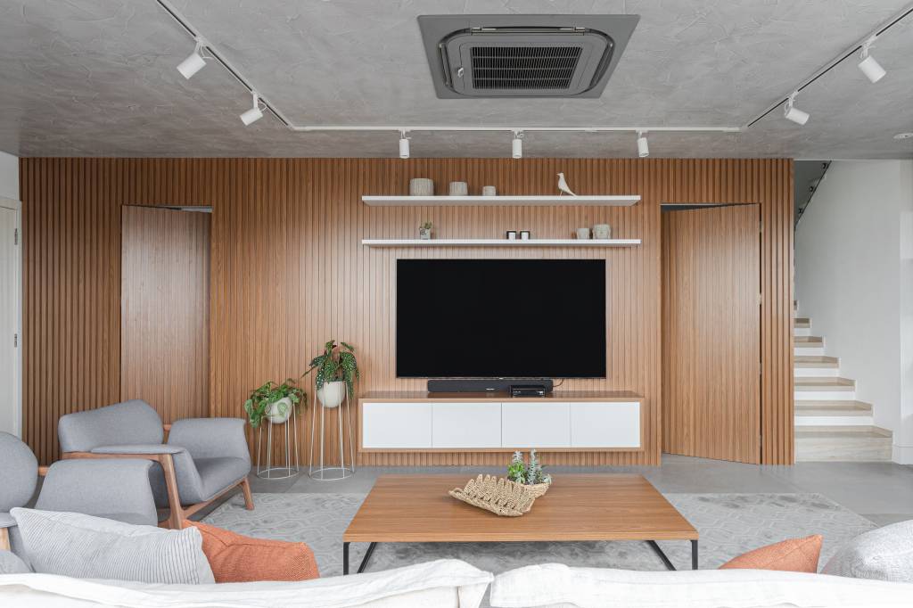ape-150m-hidromassagem-integrada-living-leticia-nobrega-08-sala-tv-spot Sala de estar com parede revestida de painéis de madeira e iluminação com trilho de spots.