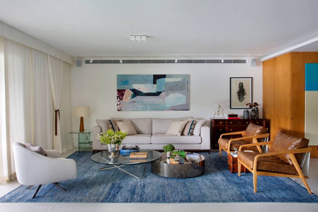 ape-210m-varanda-20m-area-de-lazer-bancada-gourmet-studio-021-arquitetura-08 Sala de estar com sofá claro, tapete azul, quadros e cadeiras de madeira.