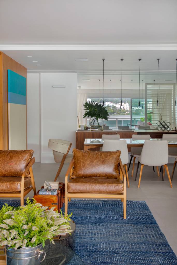 ape-210m-varanda-20m-area-de-lazer-bancada-gourmet-studio-021-arquitetura-11 Sala de jantar integrada com sala de estar; poltrona de couro, tapete azul e mesa de jantar com cadeiras.