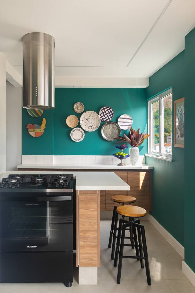 azul-verde-marcam-ape-81m-cozinha-integrada-bancada-espacosa-ketlein-amorim-10-cozinha Cozinha com parede verde, backsplash de azulejos brancos e coifa.
