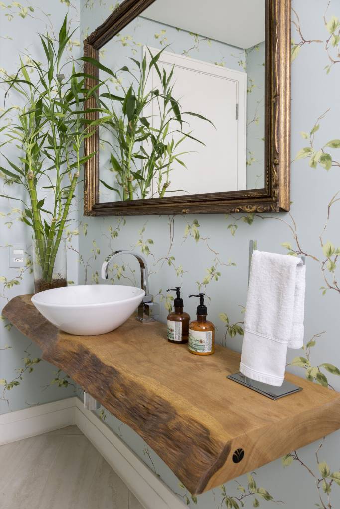 Lavabo com papel de parede floral, bancada em madeira e cuba solta branca.