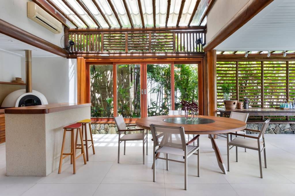 casa-400m-teto-retratil-deck-estante-embaixo-escada-11-area-gourmet Área gourmet com mesa redonda, churrasqueira, piso de porcelanato.