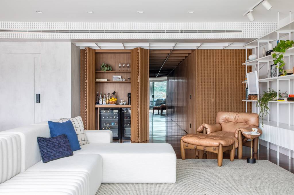 cobertura-320m-varanda-integrada-portico-muxarabi-studio-plano-arquitetura-14 Sala de estar com sofá branco e bar escondido em armário.